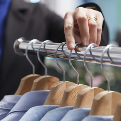 Shopping mall boutique seller hand adjusting and exploring apparel on rack closeup. Seller arm managing merchandise inventory and counting clothes in stock while working in outlet